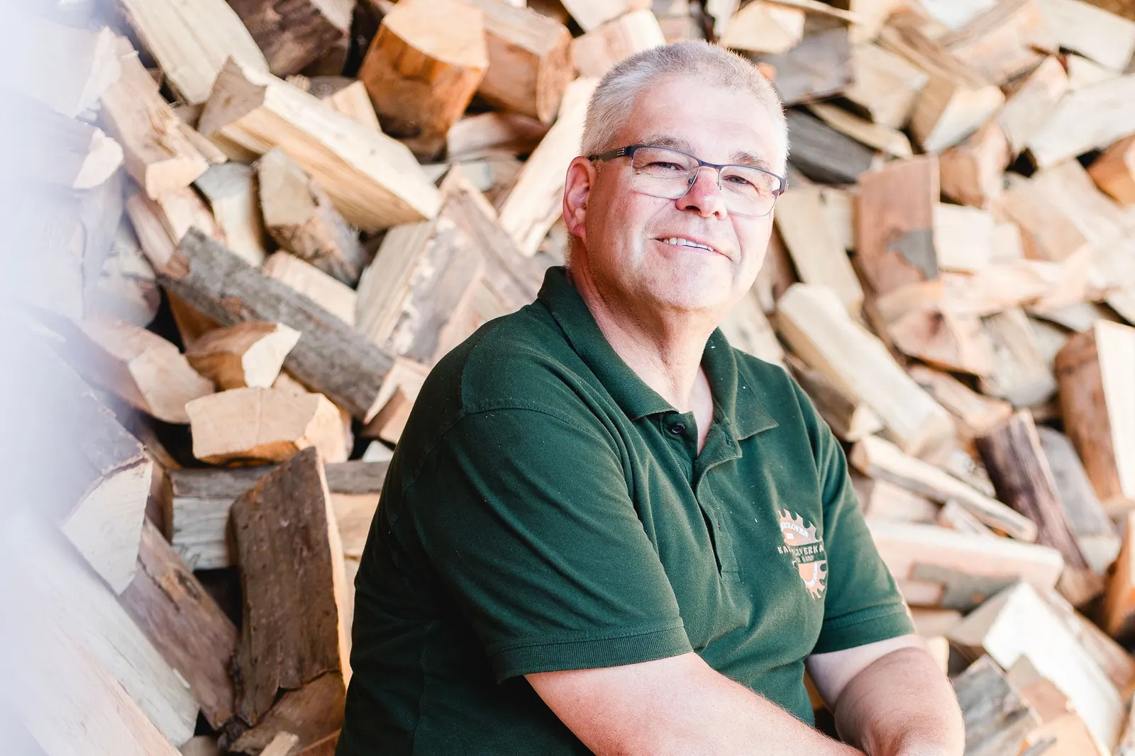 Karsten Garbe sitzt vor einem Vorrat gespaltenen Kaminholzes